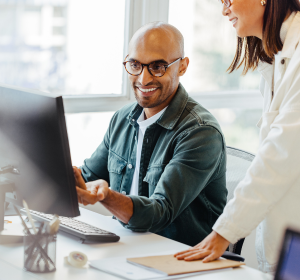 Two people talking in front of computer monitor